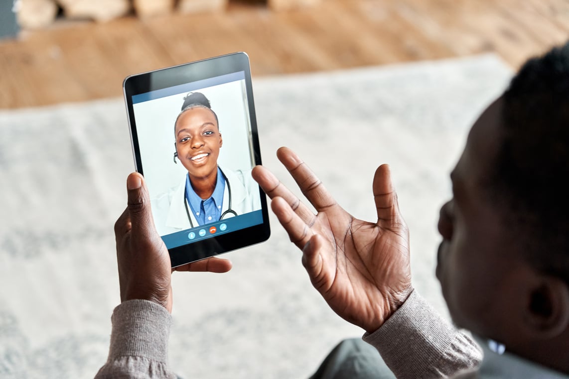 Over Shoulder View of African Patient Video Calling Virtual Doctor on Tablet.